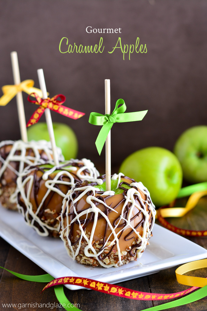 Caramel Apples drizzled with chocolate and dipped in nuts, sitting on plate and ribbons and green apples scattered around on the table.